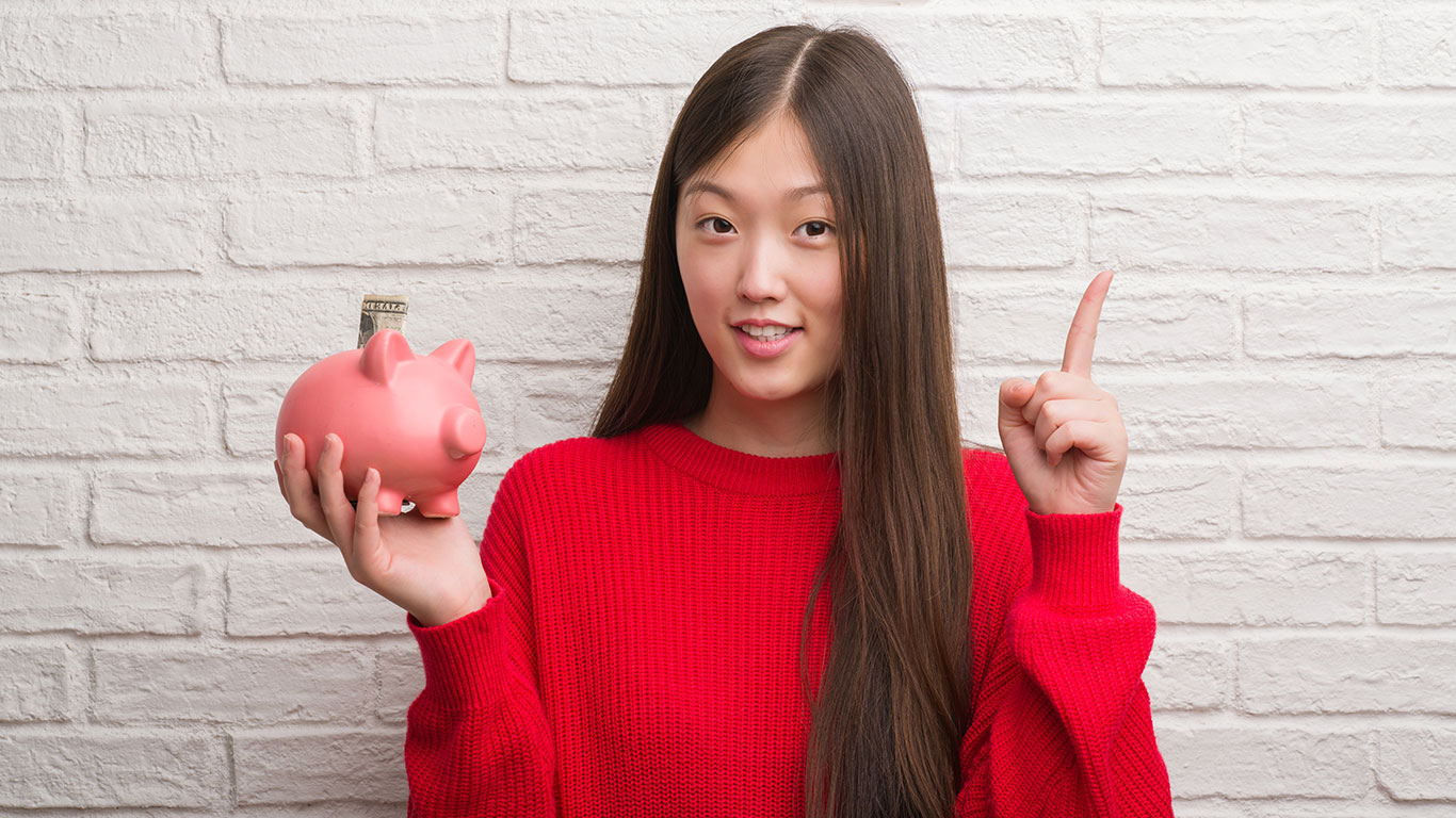 Beautiful Smiling Girl in red top Holding a pink piggy bank.