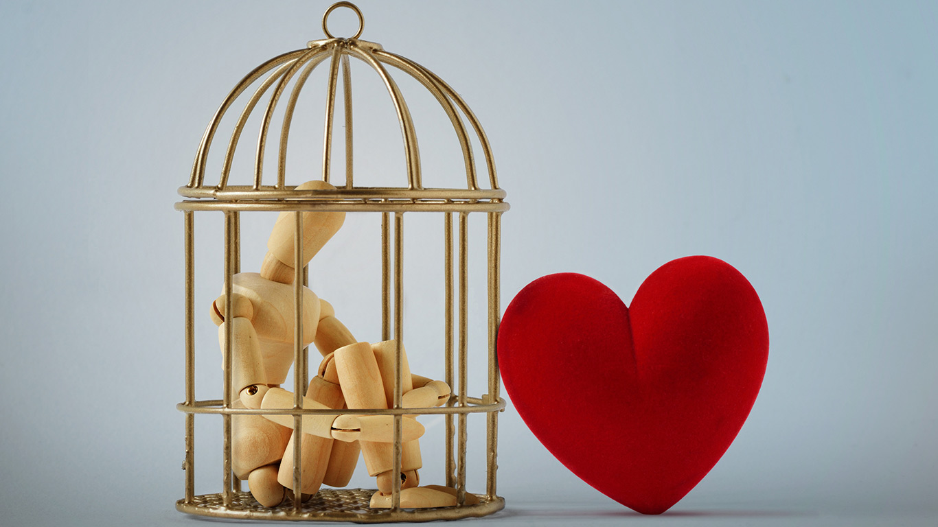 wooden figure sitting in golden cage with a valentine outside the cage.